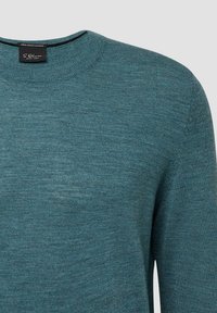 Turkusowy sweter wykonany w 100% z wełny merino, z okrągłym dekoltem i drobno dzianiną. Metka wyraźnie widoczna wewnątrz dekoltu.