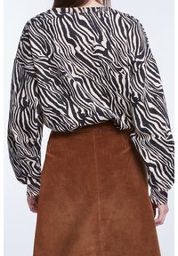 Sort og creme zebra-stribet oversized skjorte med lange ærmer, parret med en brun kordfløjlsskjorte, der viser ribbet tekstur.