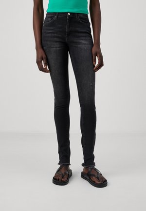 Sorte skinny jeans med en falmet tekstur, frynset kant og femlommesdesign, kombinert med sorte flip-flops og en grønn topp.