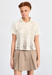 Leopardmönstrad polo med korta ärmar och krage, gjord av lätt tyg. Kombinerad med en veckad beige kjol.