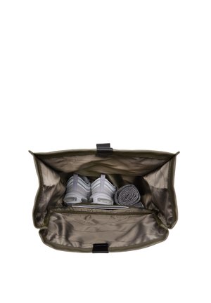 Sac en tissu vert avec un intérieur argenté, contenant des chaussures de sport grises, une serviette roulée et un objet plat dans un compartiment zippé.