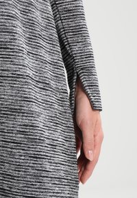 Maglione a righe grigie con una vestibilità morbida, realizzato in materiale tricot morbido. Presenta una fessura laterale sulle maniche e una sottile texture nel tessuto.