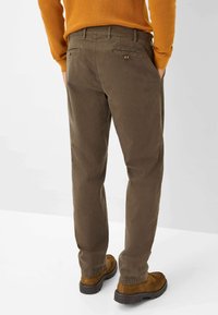Bruine katoenen broeken met een rechte pasvorm, voorzien van achterzakken met knopen en contrasterende stiksels. Gecombineerd met bruine schoenen.