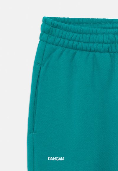 Pantalones de chándal turquesa con cintura elástica, bolsillos laterales y un logo blanco en el dobladillo inferior. Fabricados en suave tela de algodón con una textura lisa.