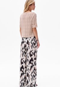 Kremowy sweter robiony na drutach z wzorem liści, w połączeniu z luźnymi spodniami w wzory w kolorach beżowym, brązowym i czarnym.
