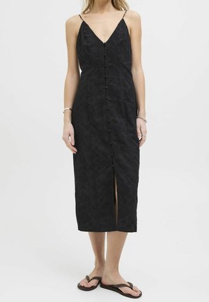 Woman wearing a sleeveless black midi dress with front buttons and a front slit, paired with black flip-flop sandals on a white background.