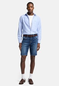 Lysblå skjorte med knapper, hvid t-shirt under, blå denim shorts, brun bælte, brune loafers og hvide sokker. Uformel påklædning.