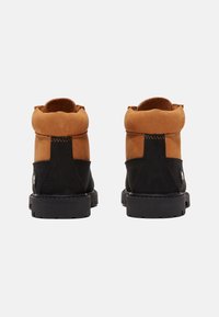 Botines de ante marrón y negro con punta redonda, cuello acolchado y suela de goma negra texturizada. Presenta costuras y detalle de logotipo.