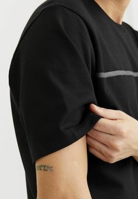 Sort kortærmet t-shirt lavet af bomuld, med en vandret grå stribe over brystet og en afslappet pasform.
