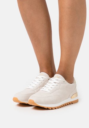 Světlé béžové semišové tenisky s bílými tkaničkami, texturovanou gumovou podrážkou a zlatými detaily. Disponují zaoblenou špičkou a polstrovaným patou.