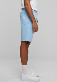 Light blue cotton shorts with an elastic waistband, side pockets, and a small logo patch, paired with white sneakers and socks.