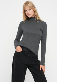 Hallide pika varrukaga turtleneck pluus pehmest kangast, mis on kombineeritud kõrge vöökohaga mustade teksadega. Lihtne disain, keha lähedane siluett, minimaalne detailsus.