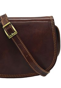 Sac bandoulière en cuir marron avec une finition lisse, des coutures contrastées et un accent de boucle en laiton sur la sangle réglable.