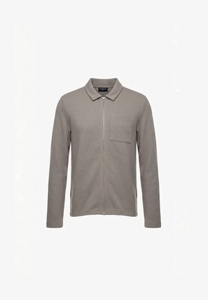 Chemise grise à manches longues avec fermeture éclair, col et poche poitrine, fabriquée en tissu texturé, présentée sur un fond blanc.