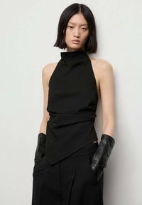 Črna halter bluza z visokim ovratnikom, ki ima drapiran dizajn in asimetričen rob, v kombinaciji z elegantnimi črnimi usnjenimi rokavicami.