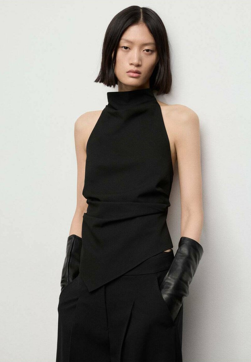 Črna halter bluza z visokim ovratnikom, ki ima drapiran dizajn in asimetričen rob, v kombinaciji z elegantnimi črnimi usnjenimi rokavicami.