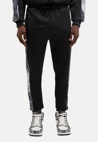 Sorte sweatpants med en tætsiddende pasform, der har teksturerede hvide grafiske mønstre langs siderne og en justerbar talje for komfort.