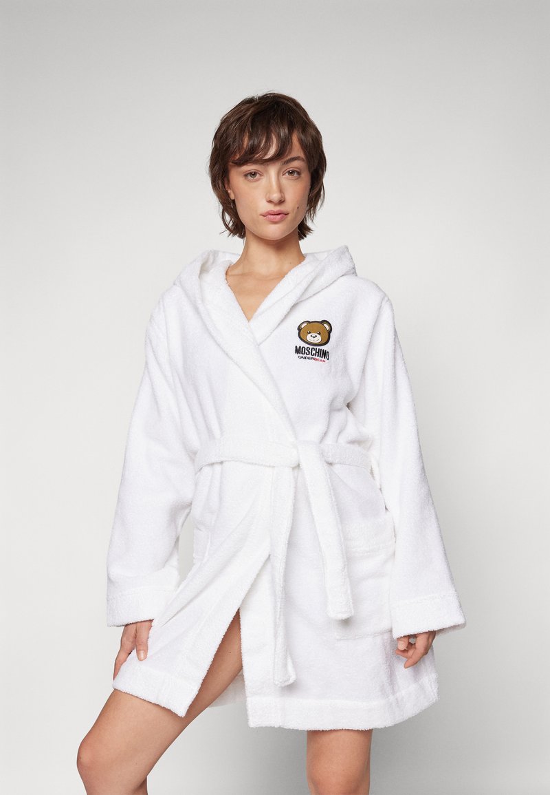 White terry cloth bathrobe with hood, tie belt, two front pockets, featuring embroidered bear logo on the left chest. Soft texture.