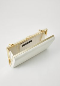 White patent leather clutch with a structured shape, featuring a gold-tone frame and clasp. Interior includes a black label.
