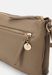 Bruine faux leren schoudertas met twee ritscompartimenten, gouden hardware accenten en een ronde merkcharme eraan bevestigd.