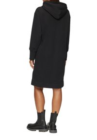 Zwarte hoodie jurk gemaakt van zachte stof. Heeft een grote capuchon en geribde manchetten. Gepaard met zwarte enkelboots met dikke zolen.