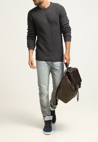 Grijze geribde trui, lichtblauwe jeans, blauwe sneakers en een bruine leren rugzak. Casual outfit met textuur en verschillende tinten.