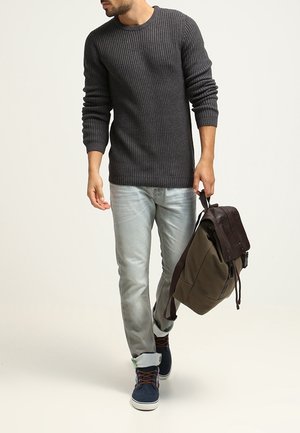 Grijze geribde trui, lichtblauwe jeans, blauwe sneakers en een bruine leren rugzak. Casual outfit met textuur en verschillende tinten.