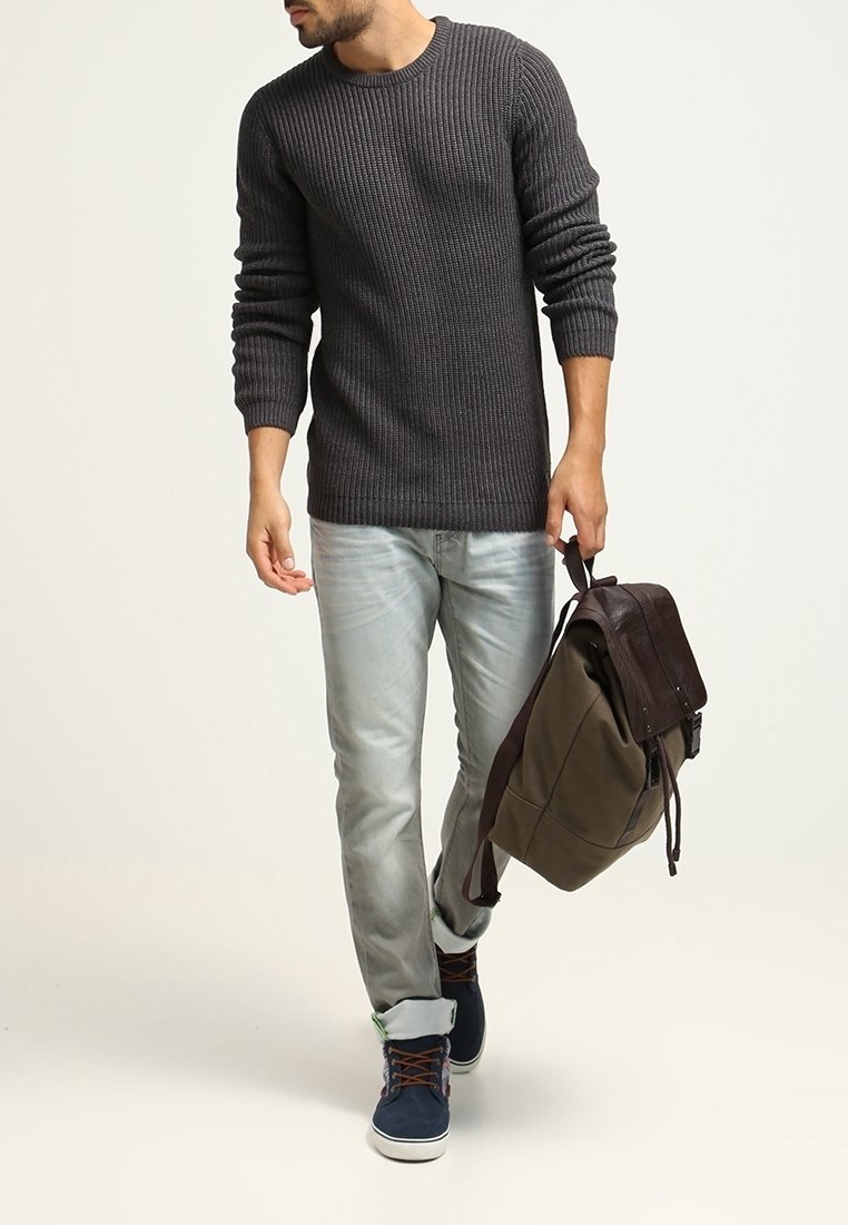 Grijze geribde trui, lichtblauwe jeans, blauwe sneakers en een bruine leren rugzak. Casual outfit met textuur en verschillende tinten.