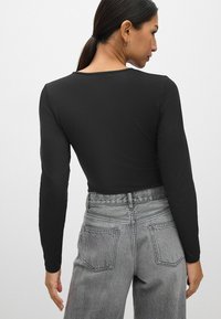 Sort langærmet top med rund udskæring, parret med højtaljede, falmede grå jeans med baglommer og en tekstureret overflade.