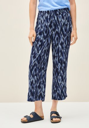 Navy blue patterned pants with a relaxed fit, featuring a wide elastic waistband and cropped length. Worn with black slide sandals.