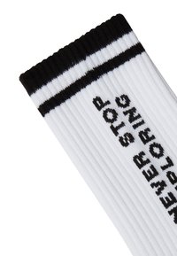 Calcetines blancos de canalé con rayas negras en la parte superior, que presentan "NO DEJES DE EXPLORAR" en texto negro en negrita a lo largo del costado.