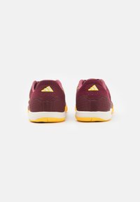 Scarpe da ginnastica color bordeaux con accenti gialli, parte superiore in mesh, coperture per tallone testurizzate e solide, e suola in gomma bianca. La vista posteriore mostra un design unico.