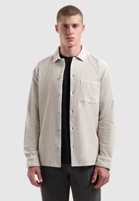 Lichtbeige corduroy overhemd met een knoopsluiting aan de voorkant, één borstzak en lange mouwen. Draag het over een zwart shirt, met een casual pasvorm.