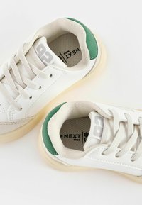 Vita sneakers med gröna accenter, läder- och mesh-material, rund tå, texturerad tunga och lätta gummisulor. Logotyp på sidan.