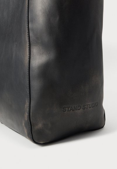 Sort lædertaske med en glat tekstur, rektangulær form og indpræget "STAND STUDIO" logo på siden. Mat finish, minimalistisk design.