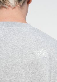 Grijze korte mouwen shirt van zachte stof, met een wit geborduurd logo achteraan bij de nek. Eenvoudig en casual ontwerp.