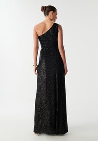 Crna haljina sa jednim ramenom, dužine do poda, ukrašena šljokicama, sa uskim korzetom i raširenom suknjom.