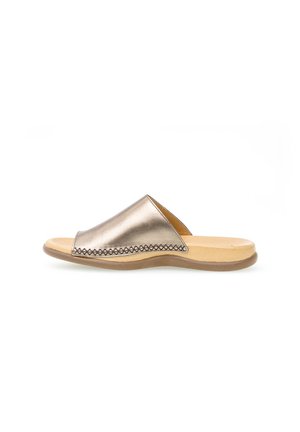Metalen gouden slip-on sandaal met een lage beige zool en een brede leren bovenzijde met decoratieve stiksels aan de zijkant.