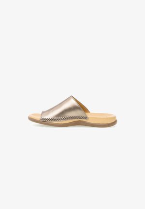 Metalen gouden slip-on sandaal met een lage beige zool en een brede leren bovenzijde met decoratieve stiksels aan de zijkant.