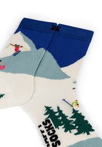 Chaussettes montantes avec une base crème et un revers bleu, ornées de motifs de montagnes, d'arbres et de skieurs aux motifs colorés, fabriquées en matériau tricoté doux.