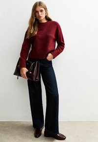 Bordeaux gebreide trui, wijde donkerblauwe jeans en glanzende bordeaux handtas. Gelaagd, ontspannen pasvorm met ribgebreide manchetten en zoom. Brown schoenen maken de look af.