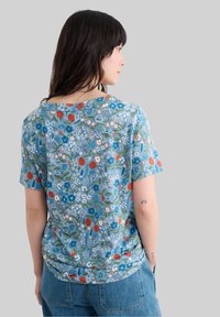 T-shirt à manches courtes bleu à motifs floraux, mettant en avant un motif vibrant de fleurs et de feuilles, fabriqué en tissu doux avec une coupe décontractée et un col rond.