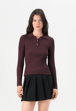 Polo a maniche lunghe color bordeaux con righe, con colletto e bottoni, abbinato a una gonna nera plissettata.
