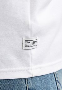 Tricou alb din bumbac cu un etichete marcate "Petrol Ind" și textul "DENIM DRIVEN SINCE '68 FLORIDA U.S.A." în negru. Cusătură vizibilă pe tiv.