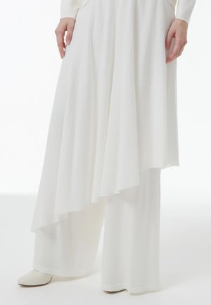 Witte gelaagde wijde broek gemaakt van zachte, gestructureerde stof. Heeft een asymmetrische zoom en een gladde, enkelhoge laars.