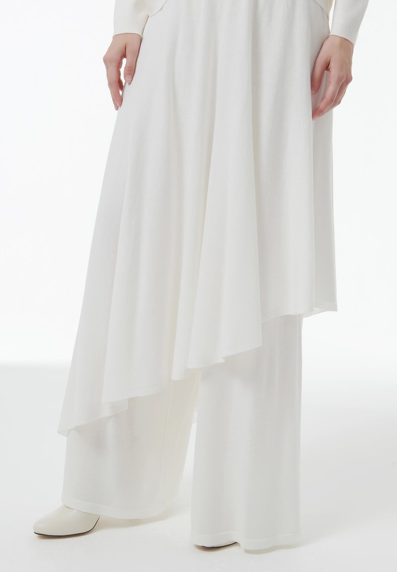 Witte gelaagde wijde broek gemaakt van zachte, gestructureerde stof. Heeft een asymmetrische zoom en een gladde, enkelhoge laars.