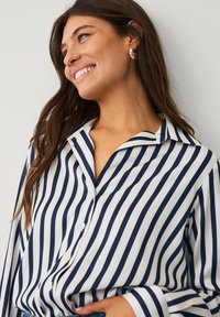 Marineblauwe en witte gestreepte blouse met een kraaghals, lange mouwen en knoopsluiting; soepele stof met een lichte glans.