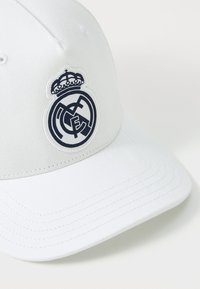 Hvit baseballcaps laget av bomull med buet skjerm, med et marineblått brodert Real Madrid-logo med en krone over.