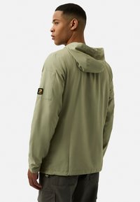 Light olive green hooded jacket with a soft texture, featuring a visible patch on the sleeve and a streamlined design.