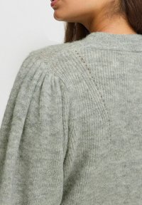 Pull en maille gris clair avec un design texturé, des manches bouffantes et des coutures détaillées au niveau des épaules.